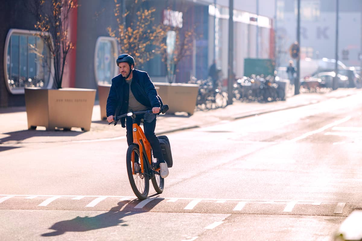 man with helmet riding his company bike in the middle of street in city