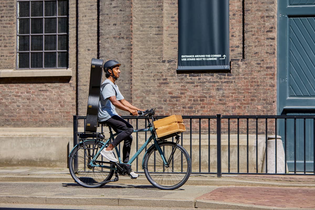 man with guitar on back rides bike along a building in summer