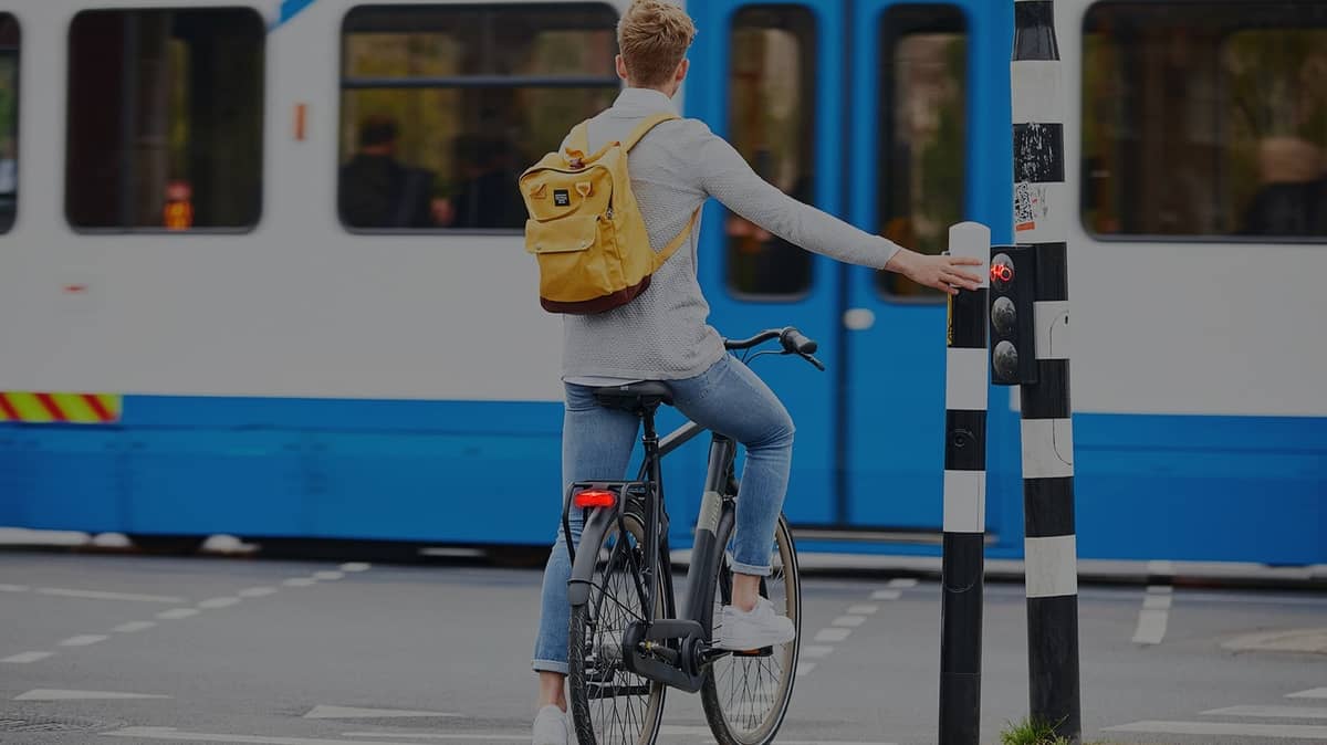 Mann mit Rucksack wartet mit Herrenrad an Ampel vor Straßenbahn