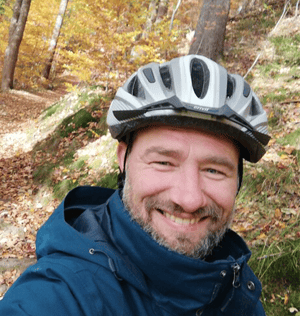 Mann mit Helm in Wald grinst in Kamera