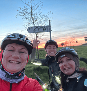 Drei Frauen mit Helm vor Sonnenuntergang lachen in die Kamera