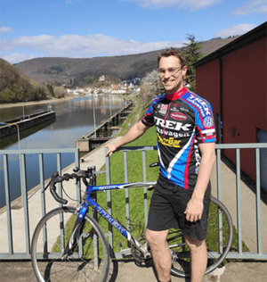 Mann auf Rennrad lachend auf Brücke vor Fluss
