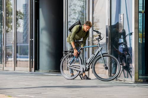 man with backpack locks bike in front of building
