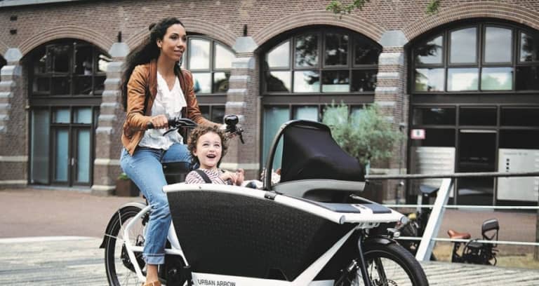 Woman on cargo bike with two kids in urban surrounding