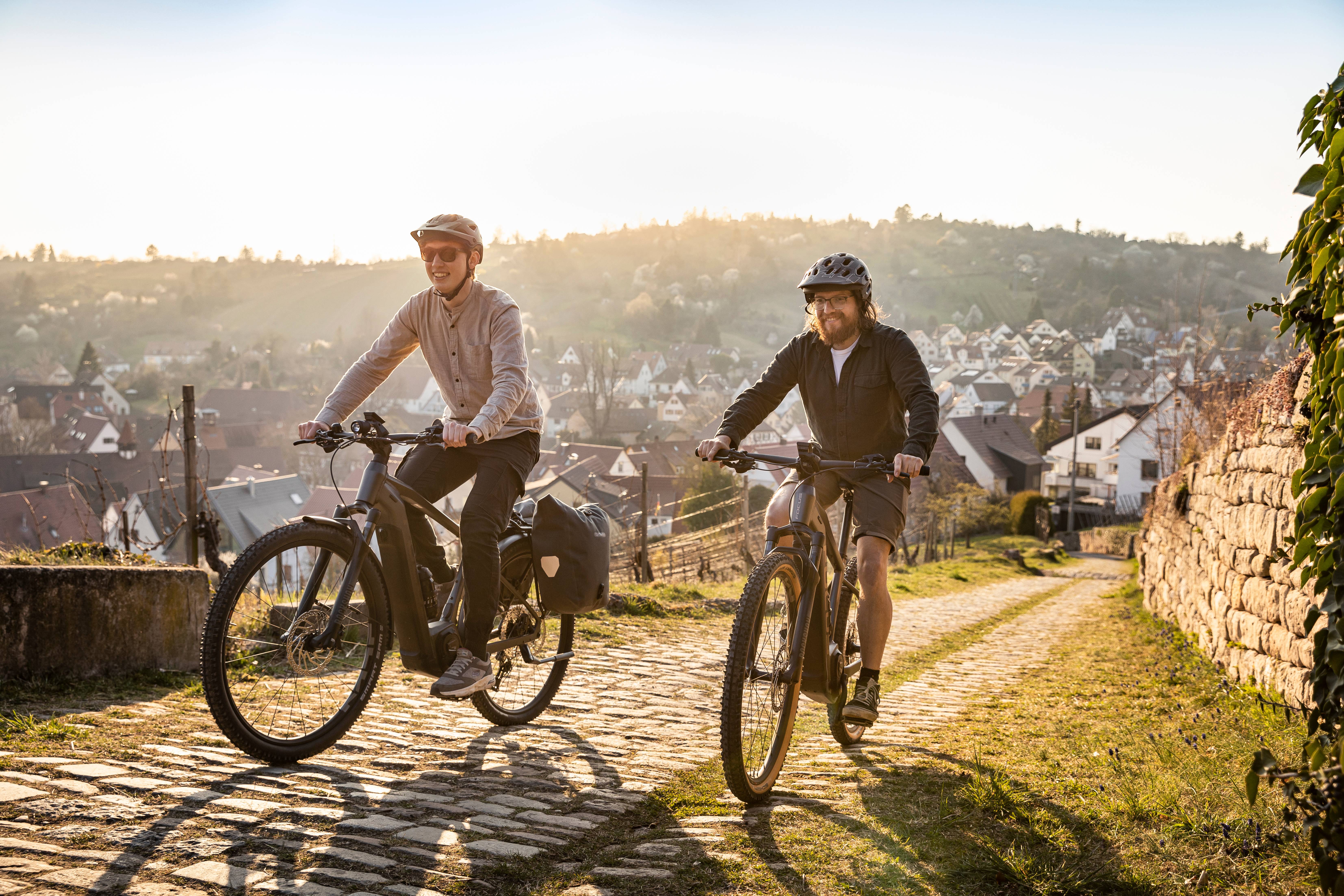Zwei Radfahrer auf Focus Fahrrädern fahren Steigung hinauf Stadt im Hintergrund
