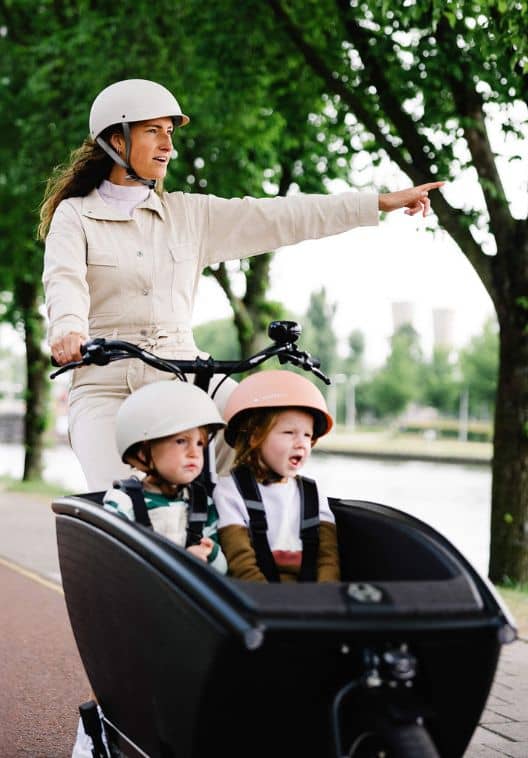 Frau mit zwei Kindern im Urban Arrow Lastenrad fährt entlang von Fluss