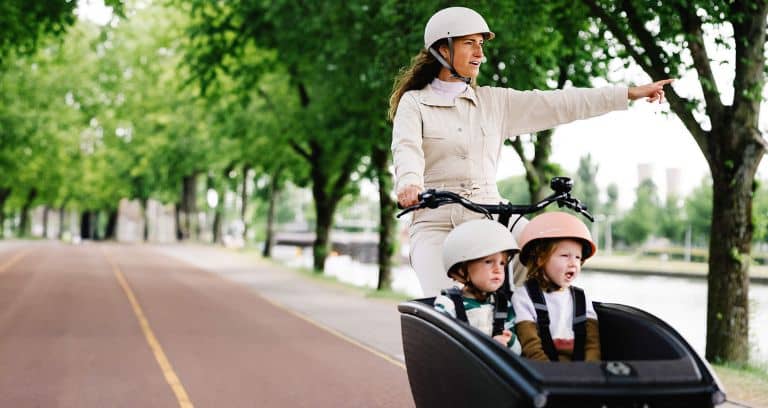 Frau mit zwei Kindern im Urban Arrow Lastenrad fährt entlang von Fluss