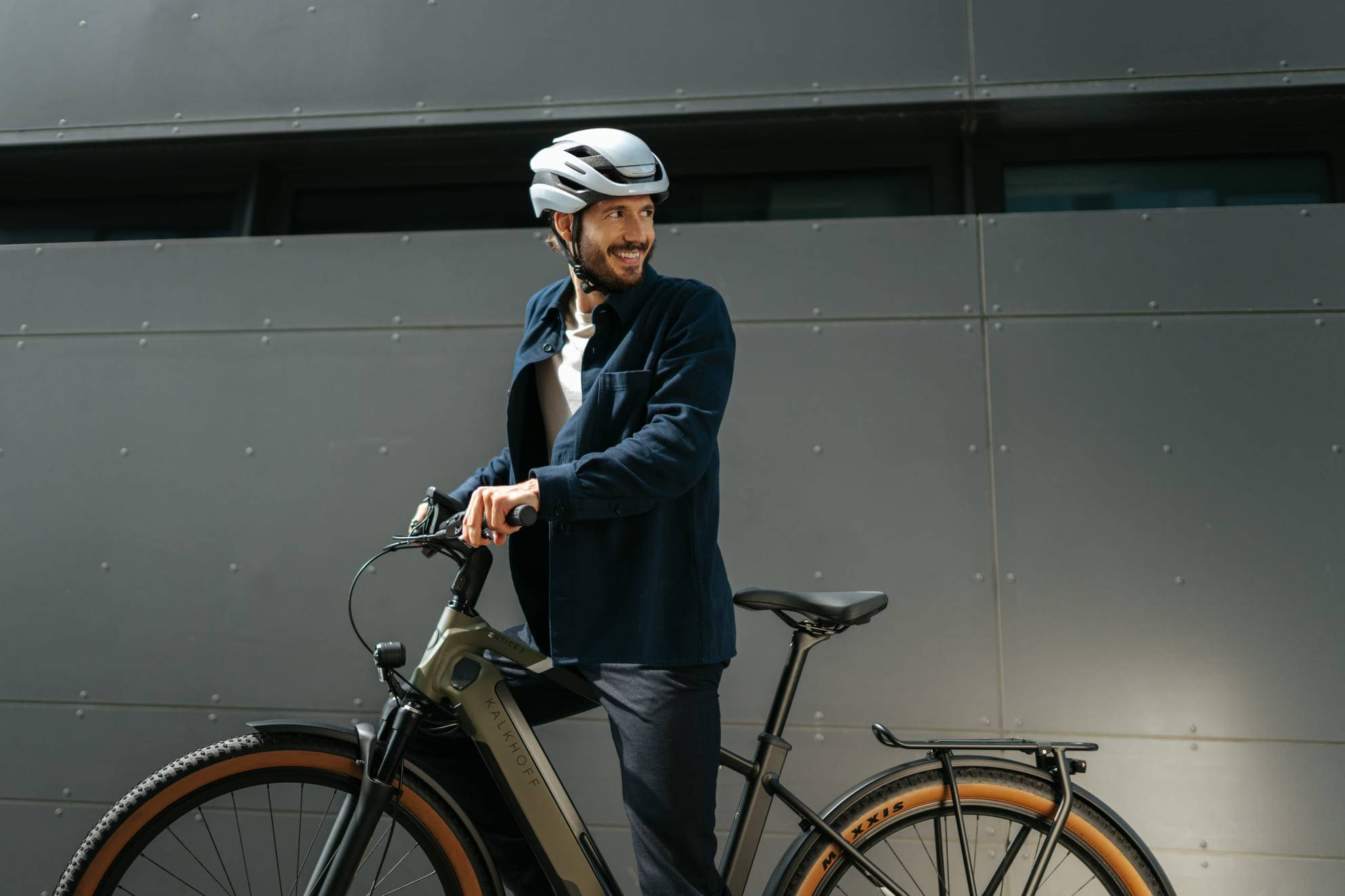 man on bike standing next to wall looking back and smiling