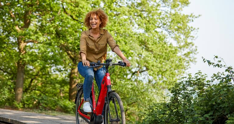 Frau auf rotem Gazelle Fahrrad lachend in grüner Umgebung